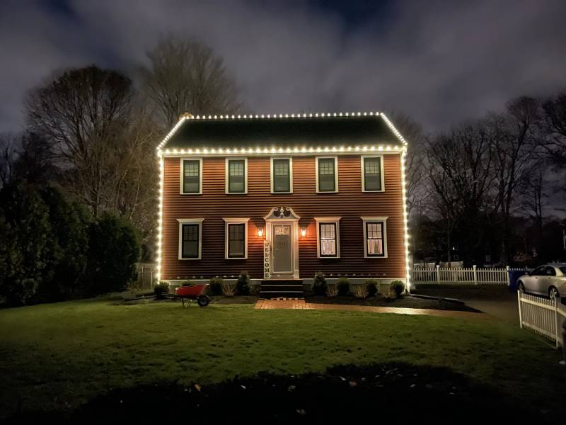 Warm white holiday roofline on a brick colonial