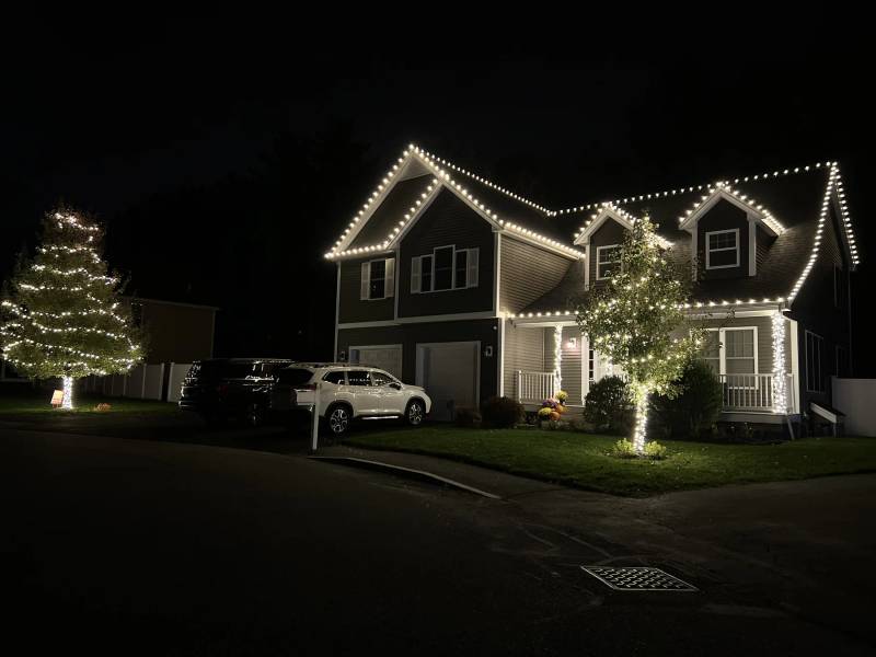 White holiday lights outlining a gabled home and front-yard tree