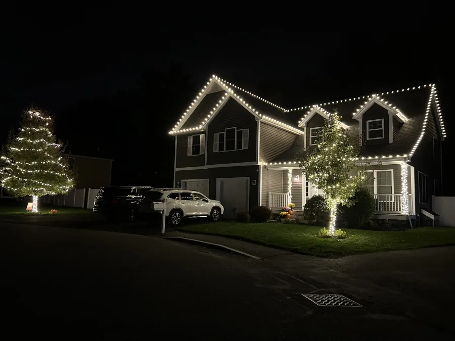 White holiday lights outlining a gabled home and front-yard tree
