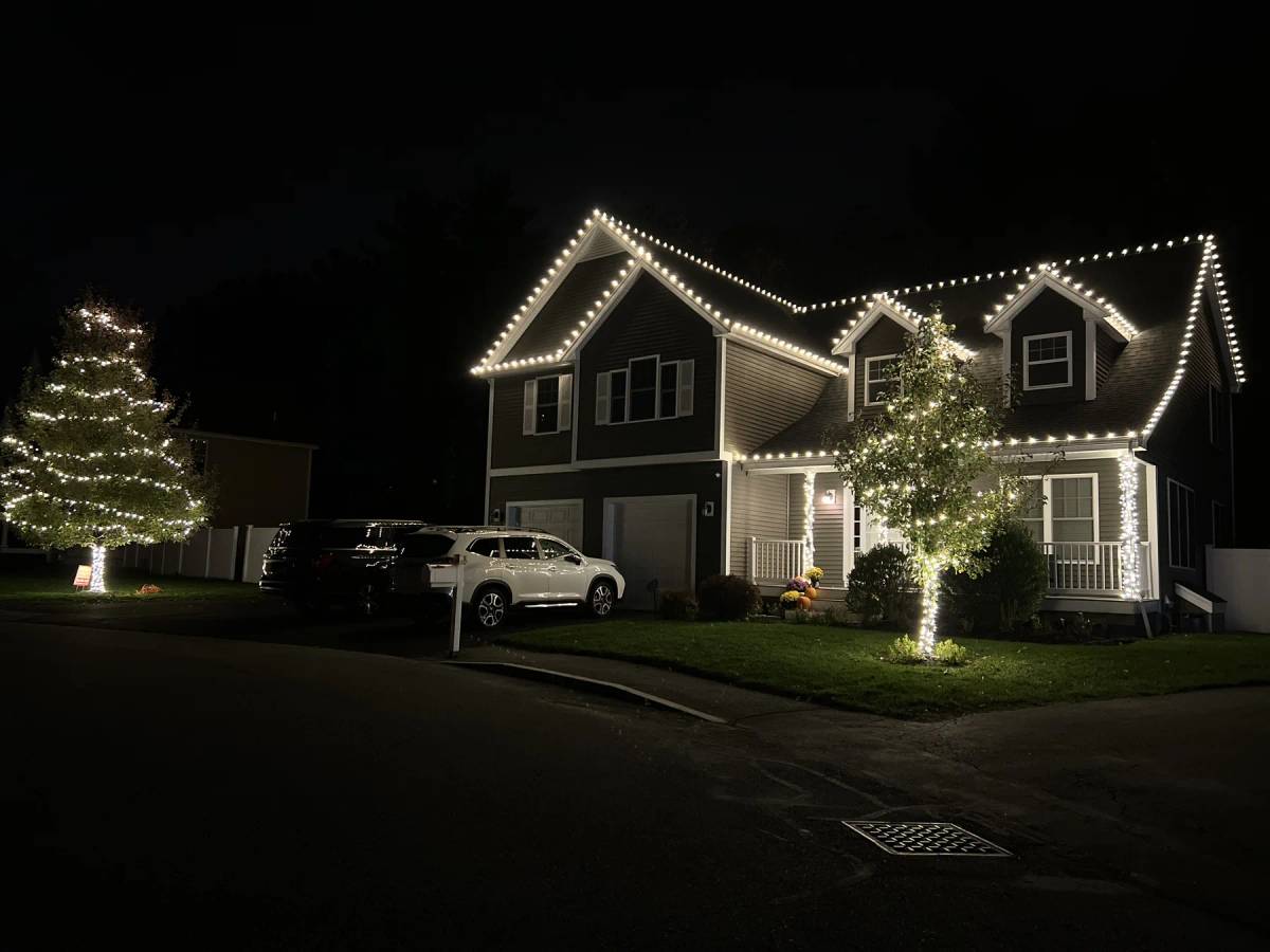 White holiday lights outlining a gabled home and front-yard tree