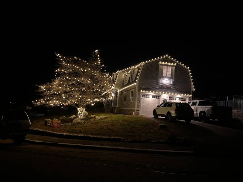 Holiday lights on a gambrel garage and tree from the street