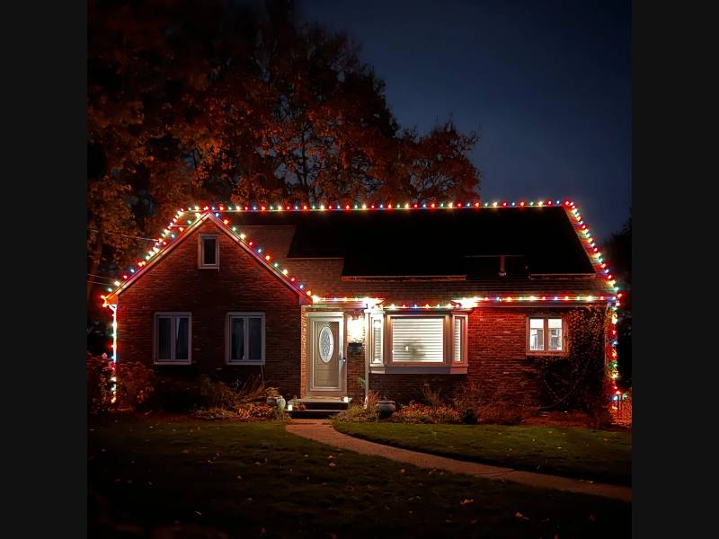 Multicolor holiday bulbs outlining a red ranch home