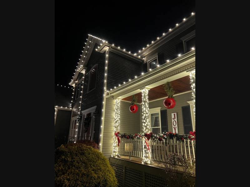 Holiday roofline lights above a porch with garland and ornaments