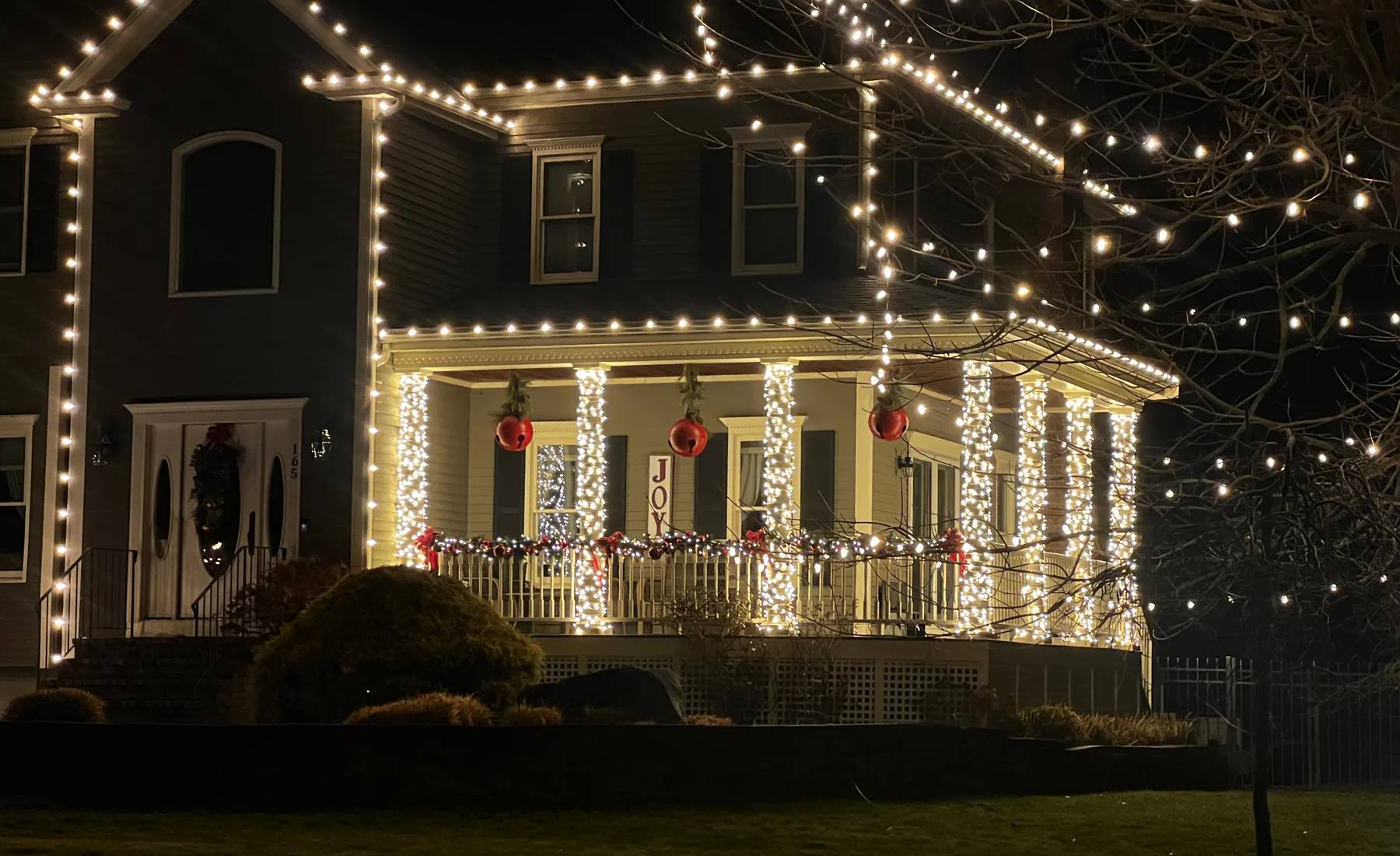 Holiday roofline lights, illuminated porch columns, garland and red ornaments