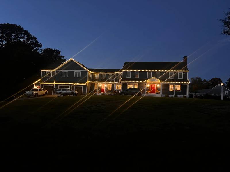 Warm holiday roofline lights on a wide home at dusk