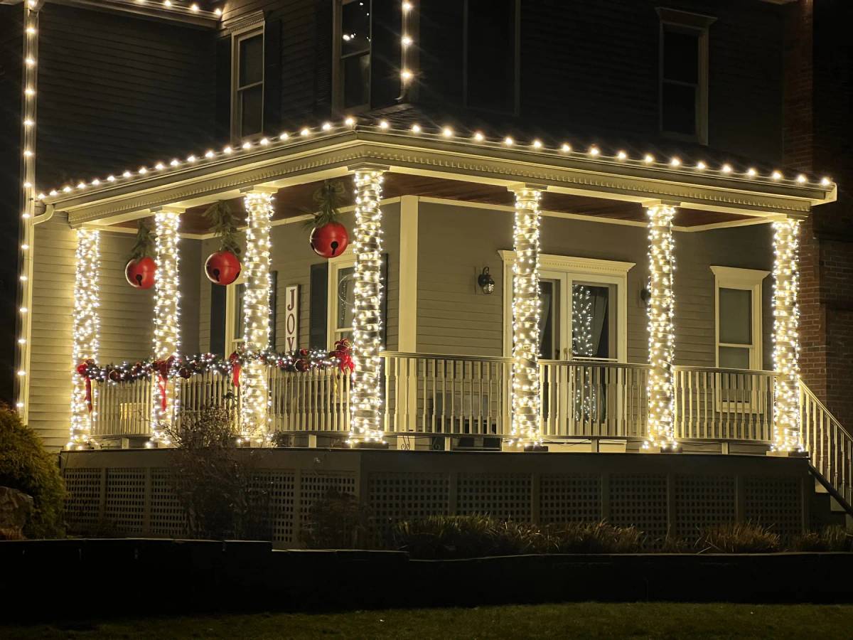Warm white holiday lights around a wraparound porch with red ornaments