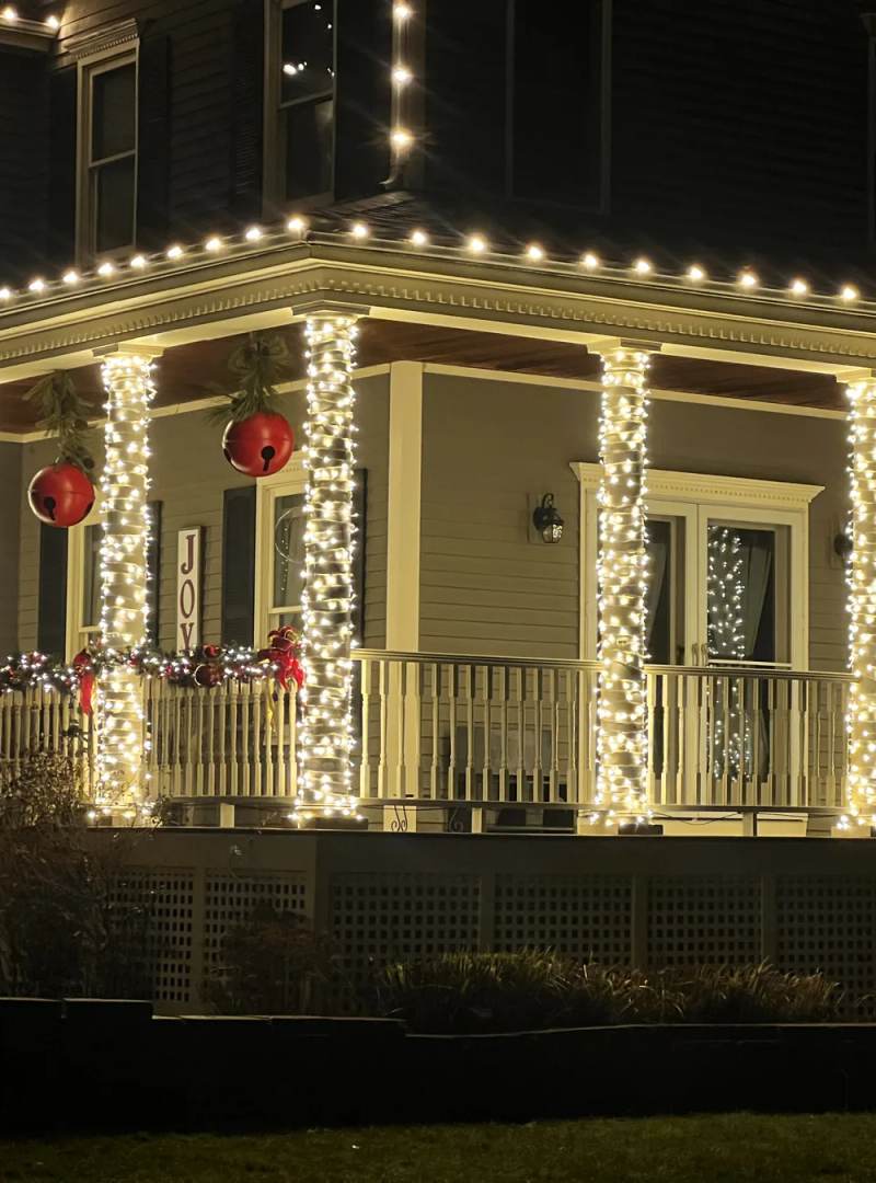 Warm white holiday lights around a wraparound porch with red ornaments
