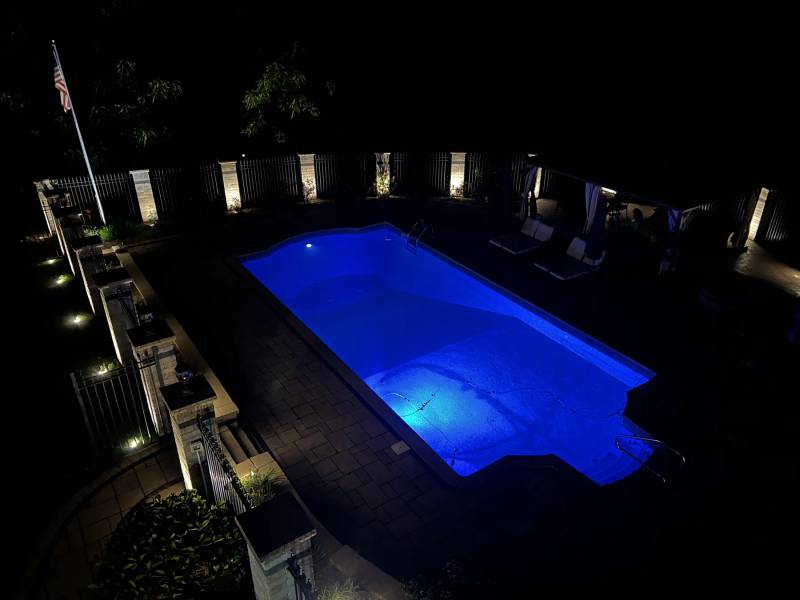 Blue-lit swimming pool surrounded by stone pillars illuminated at night