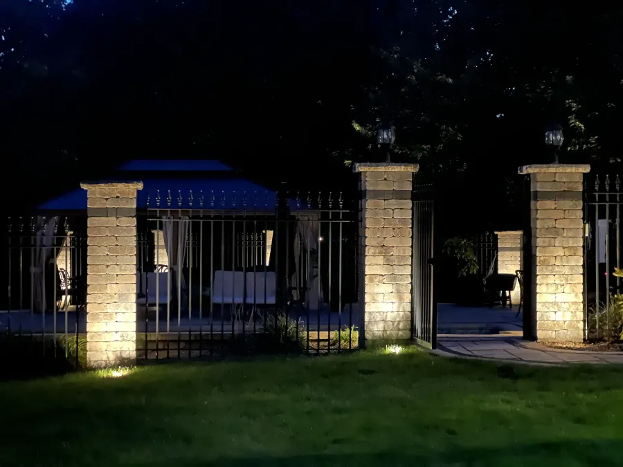 Warm uplights illuminating stone pillars on either side of a pool gate