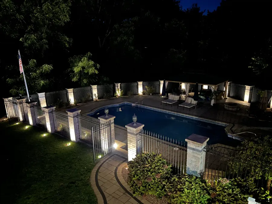 Elevated view of a pool and patio surrounded by illuminated stone fence pillars