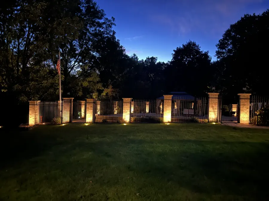 Uplighting along stone fence pillars beside a lawn at dusk