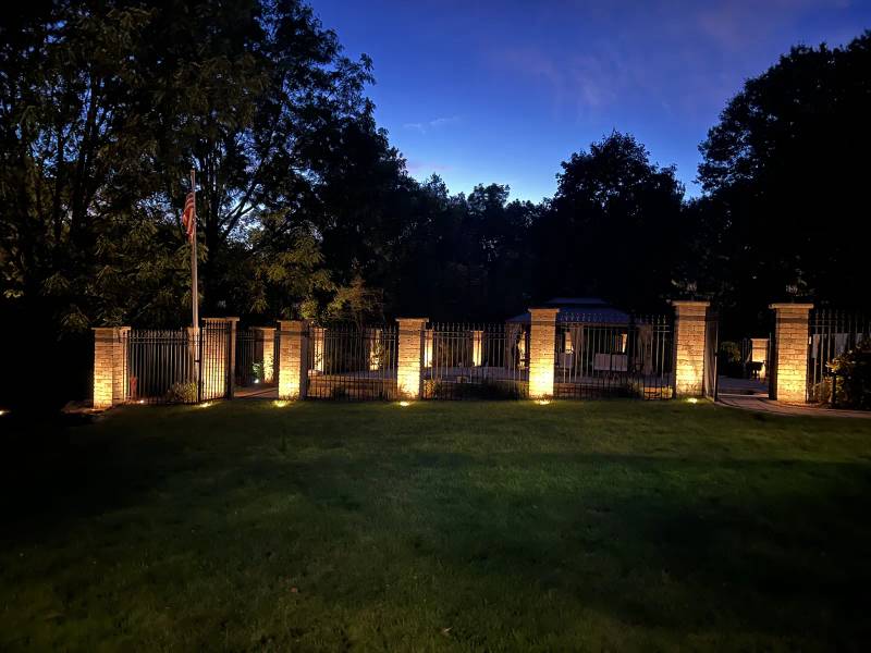 Uplighting along stone fence pillars beside a lawn at dusk