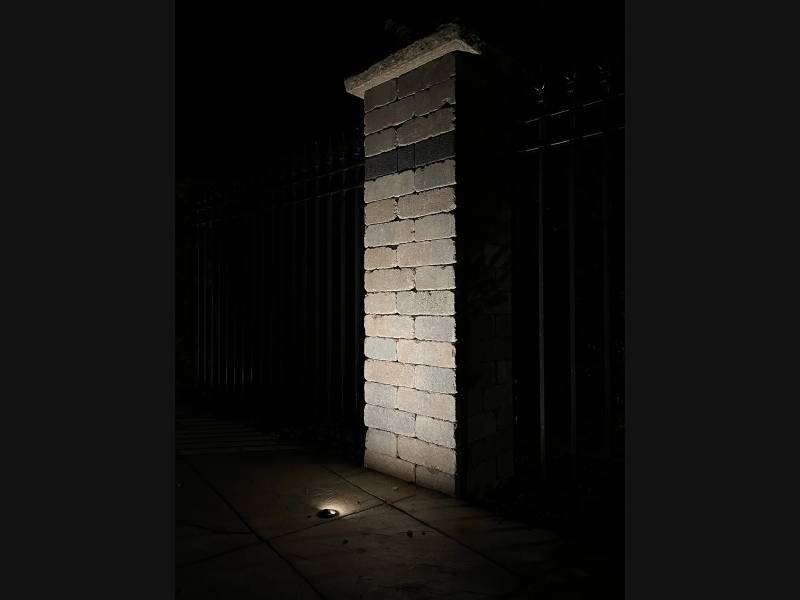 Warm uplighting revealing the texture of a stone fence pillar at night