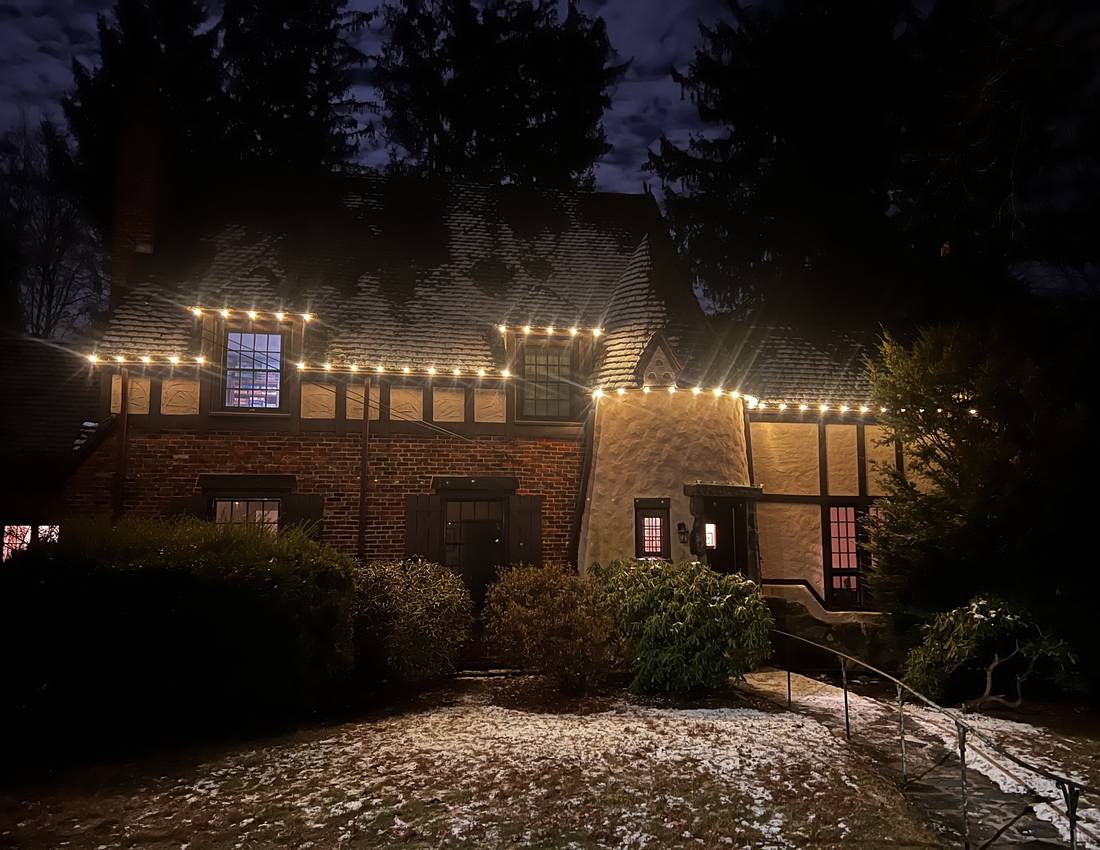 Warm holiday roofline lighting on a Tudor-style Newton home