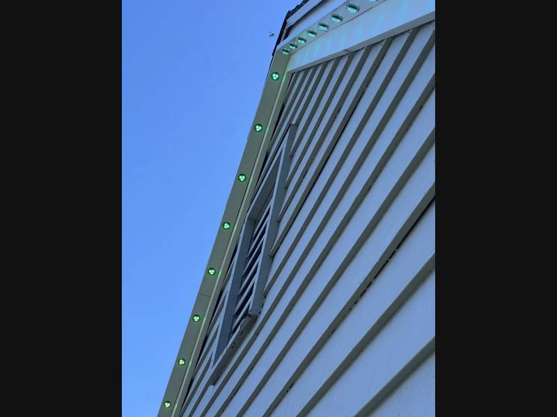 Green permanent LED lights beneath a gable in daylight